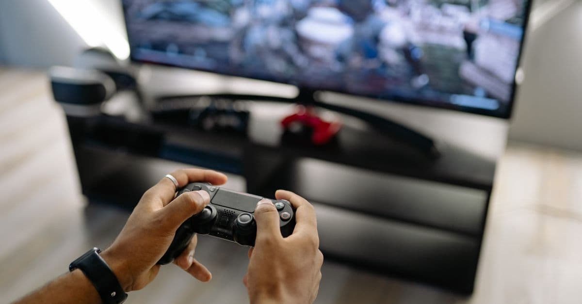 Close-up of hands holding a gaming controller while playing video games indoors.